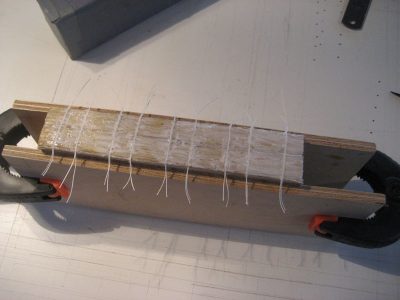 Boekblok tussen twee plankjes in de klemmen met naaigaren en overlijming voor een extra stevig verband.